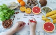 Dieting, healthy eating, slimming and weight loss concept. Close-up of diet plan list with citrus, nuts, lettuce, bananas, coconut. Woman hands writing menu