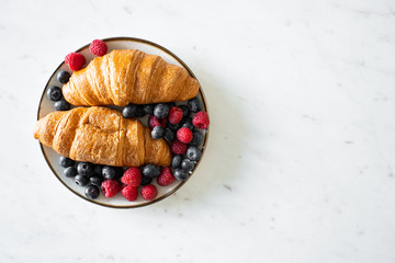 a bowl of fresh fruit and two croissants on marble table