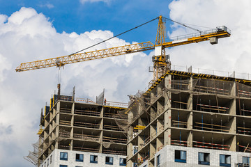 One high crane against a house and sky during the construction phase. Industry concept for low-income young families. Mortgage, business, real estate loan.