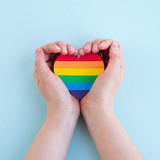 Fototapeta Tęcza - LGBT rainbow flag heart shape in woman hands. Pride month, love and tolerance concept. Top view