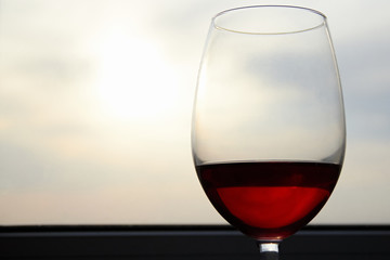 Close-up of a glass glass of red wine against a blurred background of the sky and sunset in the evening. Concept of romantic holidays