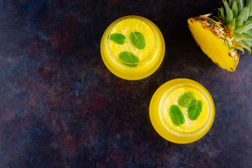 Wall Mural - Pineapple cocktail on a dark background. Cold pineapple cocktail with mint. Summer tropical cocktail on a black background. Healthy drink. Top view. Copy space