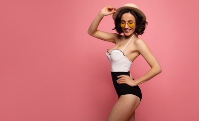 Portrait of a gorgeous trendy fit woman in swimwear while she enjoying rest with sunlight isolated over pink background. Travel, tourism, journey, trip, tour, summer concept