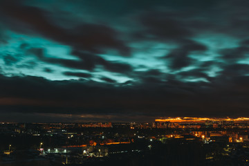 Twilight landscape of dark blue sky with black clouds and city lights. Scenic sunset. Panorama of night town. Dramatic and gloomy cityscape. Long exposure with cloud movement