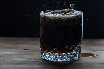 glass with a drink of dark color side view, splashes and foam from the drink. Selective focus