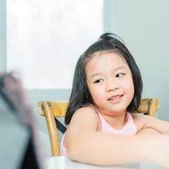 Wall Mural - Asian girl student online learning class study online with video call to teacher, Happy young girl reading story book online and looking at tablet at home.Covid-19 coronavirus.Social distancing.