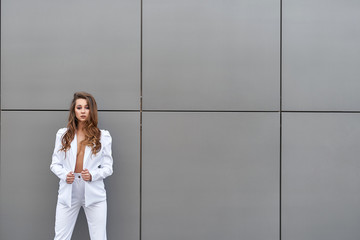 Beautiful businesswoman stands in front of a wall in a white suit