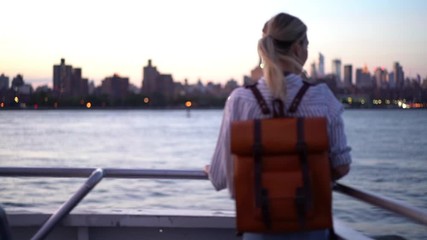 Wall Mural - Back view of trendy dressed female tourist enjoying evening excursion from water boat, carefree hipster girl with backpack discovering metropolitan city during vacations for recreation
