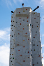 Mobile Rock Climbing Wall With Hand And Foot Grips In Red, Blue And Yellow Colour. The Tall Structure Has Safety Lines Handing Down On Three Sides. 