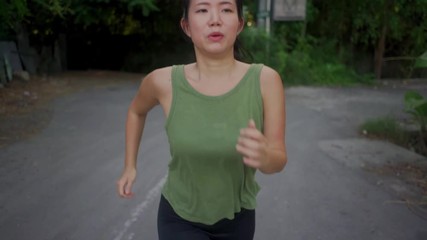 Wall Mural - outdoors running workout - slow motion tracking gimbal young happy and dedicated Asian Chinese woman jogging at beautiful city park or countryside trail enjoying fitness and cardio activity