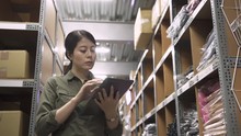 Elegant Asian Woman Manager Holding Digital Tabelt In Warehouse. Wholesale Logistic People And Export Concept. Female Business Owner Using Touch Pad Computer In Distribution Stockroom Indoors.