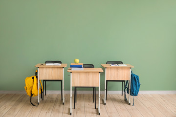 Canvas Print - School desks near color wall in classroom