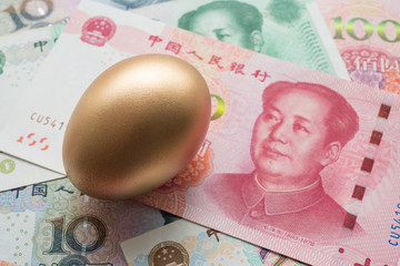 Bright golden egg on Chinese Yuan renminbi bill banknotes background. Rich, wealth, successful from stock dividend in stock market investment. Business, financial, investment and retirement planning 