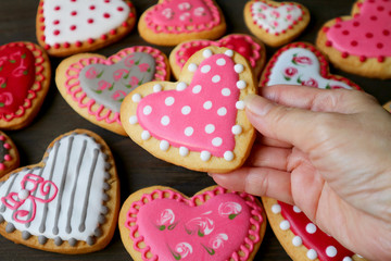 Wall Mural - Closeup dotted heart shaped royal icing cookies in hand against heap of blurry colorful heart cookies