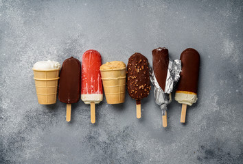 Poster - Chocolate ice cream popsicles and fruit ice cream with cones on gray cold stone background. Copy space for text.