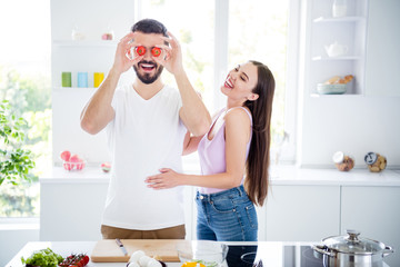 Portrait of two people spouses chef prepare organic meal dish man hold cherry tomato close cover eyes face woman humor laugh enjoy in house kitchen indoors