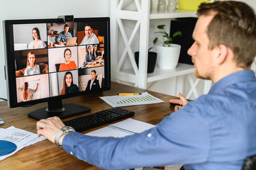 Wall Mural - Virtual conference with employees. A young man in formal shirt using pc for video call, he has video meeting with several people together. Back view. Remote work concept.