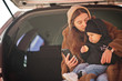 © AS Photo Family - Young mother and child sitting in the trunk of a car and looking at mobile phone. Safety driving concept.