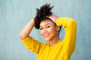 Wall Mural - Close up smiling young black woman with hand in afro hair by green background