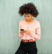 © mimagephotos - young african american woman looking at mobile phone by green background