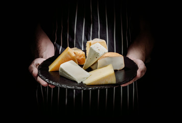 Man holding different varieties of cheese on a dark background