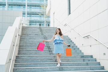 Wall Mural - Beautiful young Asian going down stairs with colorful shopping bags. Shopping and fashion concept.