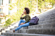 © mimagephotos - Side of beautiful young african American woman sitting on steps with mobile phone and earphones