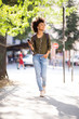 © mimagephotos - Full length young african american woman walking in city with mobile phone and earphones