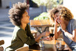 © mimagephotos - two female friends sitting at outdoor cafe with mobile phone