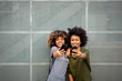 © mimagephotos - two happy young black women taking selfie with cellphones
