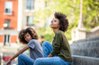 © mimagephotos - Side of two cool young african american women sitting on steps outside