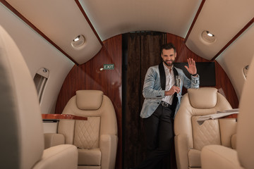 Wall Mural - selective focus of elegant, handsome man waving hand and holding glass of champagne in private plane