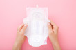 Young woman hands holding opened white sanitary towel with wings on light pink table background. Pastel color. Closeup. Point of view shot. Top down view.