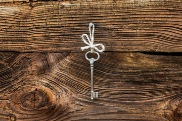 Old rusty key hanging on a nail on wooden wall background. Vintage style