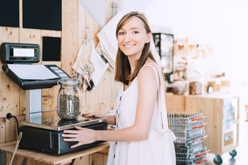 Girl weighs glass jar with hemp seeds in zero waste shop