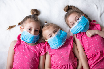 Three happy girls in pink dresses and protective medical masks. Protection against the coronavirus and influenza pandemic, home quarantine