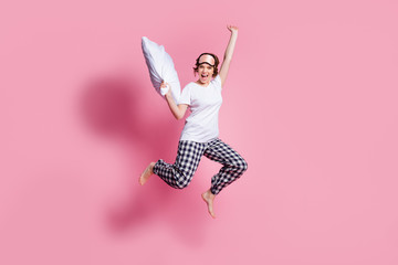 Full length photo of funny cheerful lady jump high up pillow fight rejoicing party wear sleep mask white t-shirt plaid pajama trousers barefoot isolated pink color background