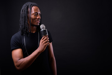 Wall Mural - Portrait of young handsome African man with dreadlocks using microphone