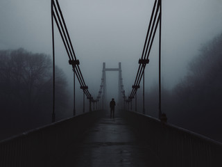 The old bridge over the river in the morning in a heavy fog and the silhouette of a man in the distance. Melancholy, depression or loneliness concept