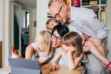 Family with three female children sittin indoors at home using digital tablet - learning, technology, togetherness concept