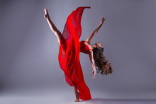 Gorgeous Young Ballet Dancer In Motion Wearing Red Dress Over Dark Grey Background