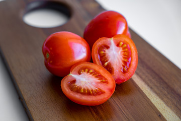 Two whole tomato and two halves of tomato isolated on a wooden cutting board on white background, closeup view