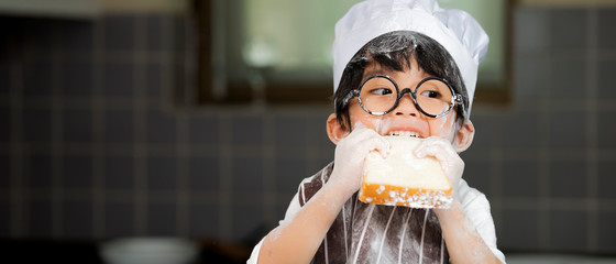 Happy cute asian  little boy in apron eating bread  in kitchen room at home