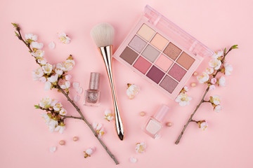 Wall Mural - Makeup cosmetics and cherry blossoms on a pink background. Close-up with space for text.