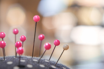 Pink pins on pincushion for sewing fabric with blurred bokeh background close-up.