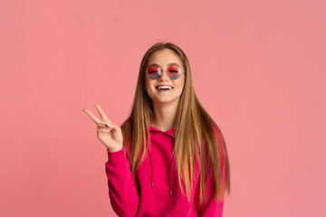 Wall Mural - Teenager girl in pink glasses shows peace sign