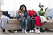 Thoughtful Black Woman Sitting On Couch Beside Lots Of Clothes And Shoes