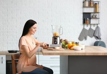 Sticker - Young pregnant woman making fruit smoothie in kitchen at home