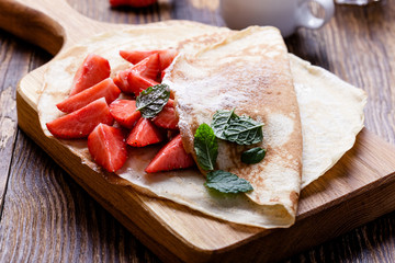 Wall Mural - Crepes with fresh strawberries on wooden cutting board