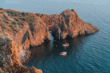 Two yachts near the grotto of Diana on Fiolenta, summer evening, people kayaking near the grotto. Recreation and travel, sea trips